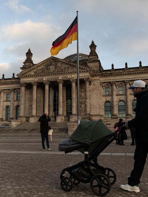 Vor dem Reichstag in Berlin, dem Sitz des Deutschen Bundestages, flanieren Menschen.