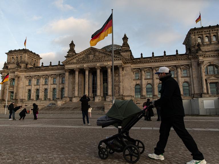 Vor dem Reichstag in Berlin, dem Sitz des Deutschen Bundestages, flanieren Menschen.