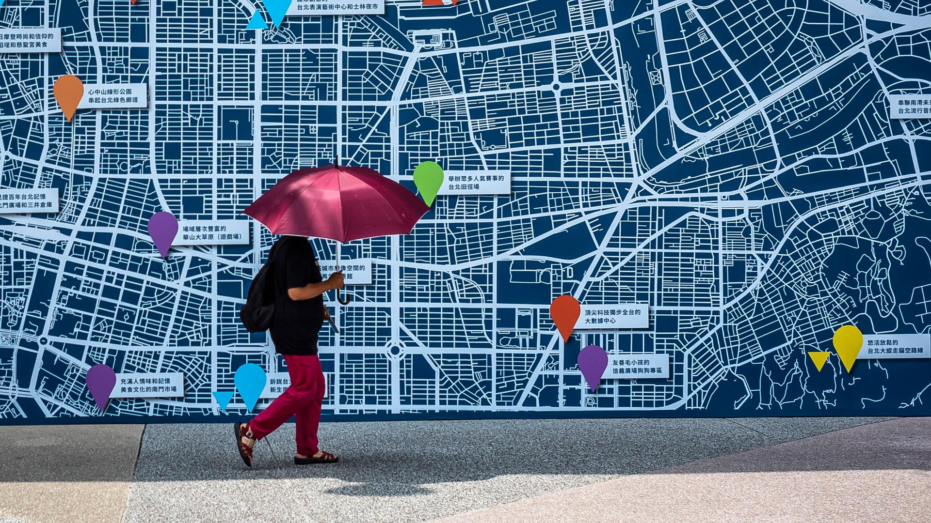 Eine Person geht mit einem roten Schirm an einer Karte von Taipei vorbei.