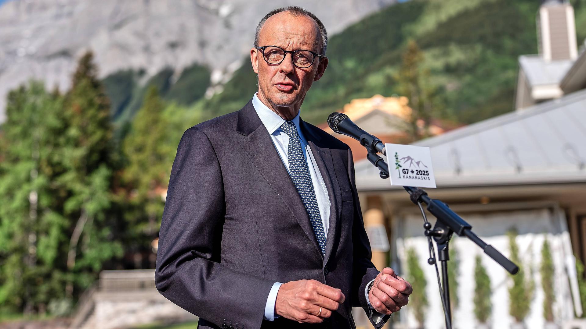 Bundeskanzler Friedrich Merz kurz vor dem Start des G7-Gipfels in Kananaskis in Kanada; er steht vor einem Mikrofon und spricht - hinter ihm sind Berge zu sehen. Bundeskanzler Friedrich Merz kurz vor dem Start des G7-Gipfels in Kananaskis in Kanada; er steht vor einem Mikrofon und spricht - hinter ihm sind Berge zu sehen.