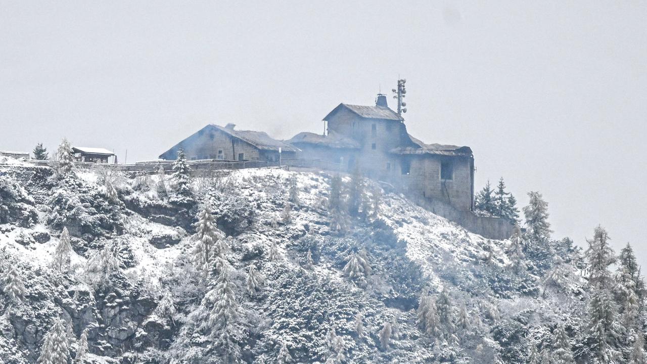 Auf einem verschneiten Berg ist ein qualmendes und durch einen Brand beschädigtes Gebäude zu erkennen.