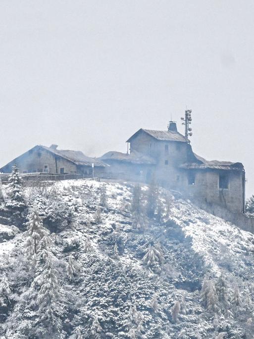 Auf einem verschneiten Berg ist ein qualmendes und durch einen Brand beschädigtes Gebäude zu erkennen.