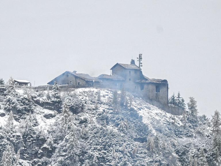 Auf einem verschneiten Berg ist ein qualmendes und durch einen Brand beschädigtes Gebäude zu erkennen.