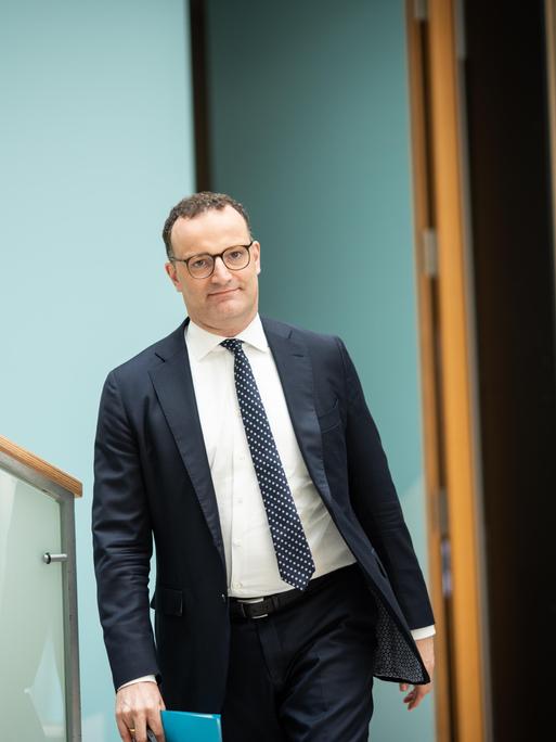 Jens Spahn läuft mit einem Hefter in der Hand im Deutschen Bundestag in Richtung der fotografierenden Person.