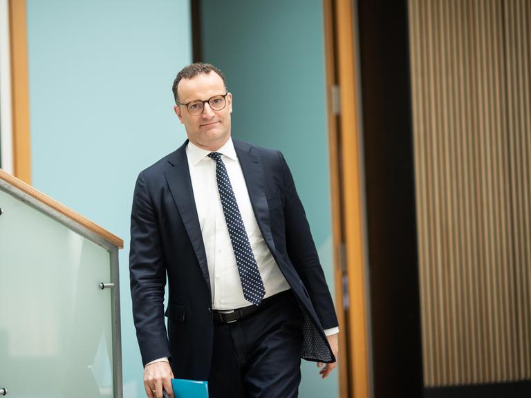 Jens Spahn läuft mit einem Hefter in der Hand im Deutschen Bundestag in Richtung der fotografierenden Person.