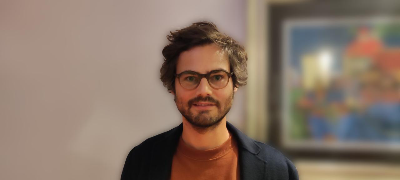 Sebastian Sevignani, ein Mann mit dunklen Haaren, Brille und kurzem Bart, in T-Shirt und blauem Sakko, schaut mit schiefem Lächeln in die Kamera.