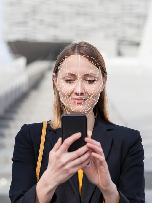 Geschäftsfrau bei Nutzung ihres Mobilfunkgerätes mit Gesichtserkennung. 