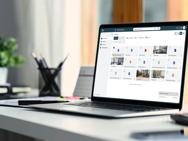 Auf einem Schreibtisch steht ein aufgeklappter Laptop. Der Bildschirm zeigt mehrere Kacheln mit Open-Source-Programmen.