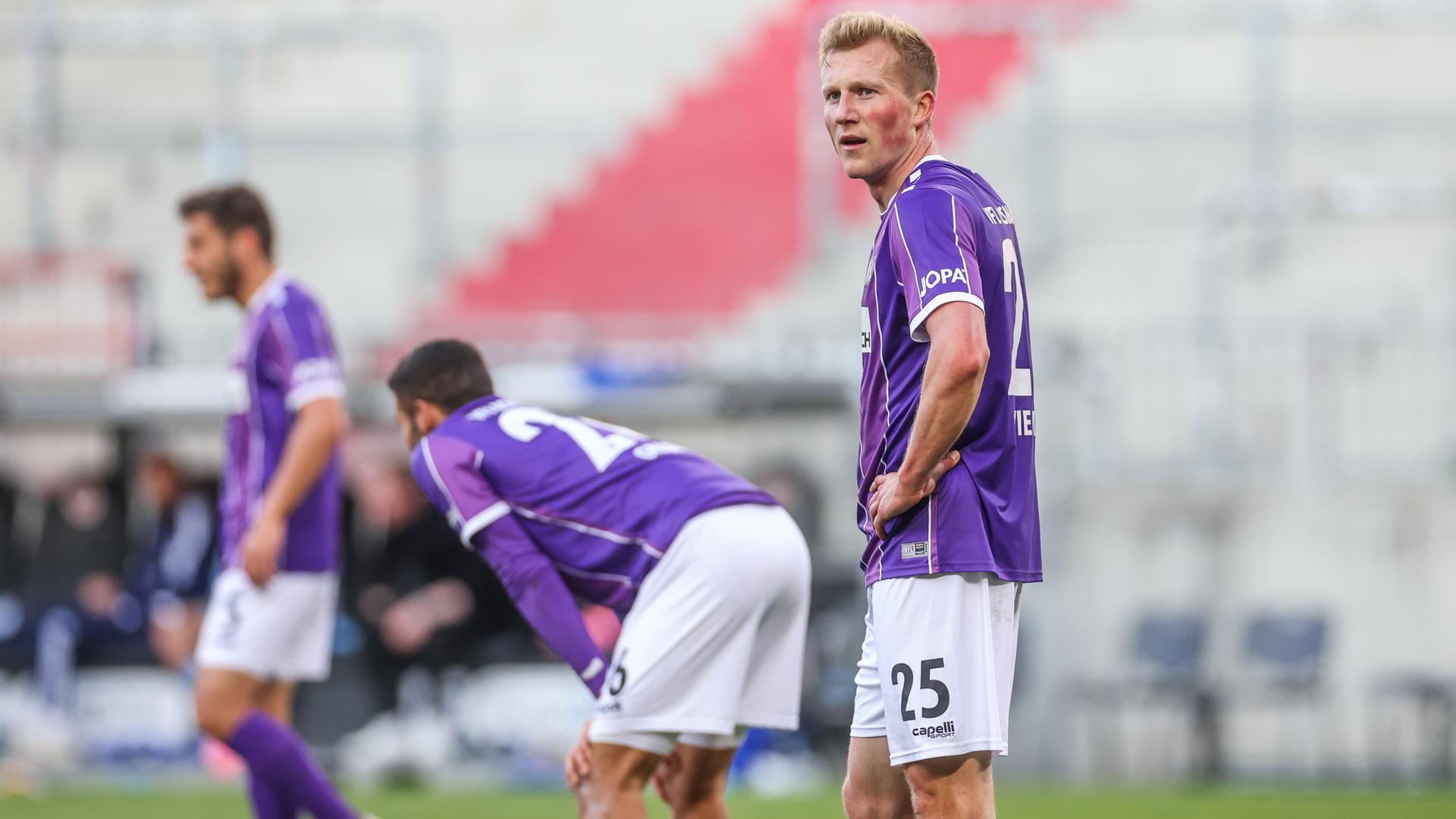 Osnabrücker Spieler in lilafarbenen Trikots stehen enttäuscht auf dem Rasen. Osnabrücker Spieler in lilafarbenen Trikots stehen enttäuscht auf dem Rasen.