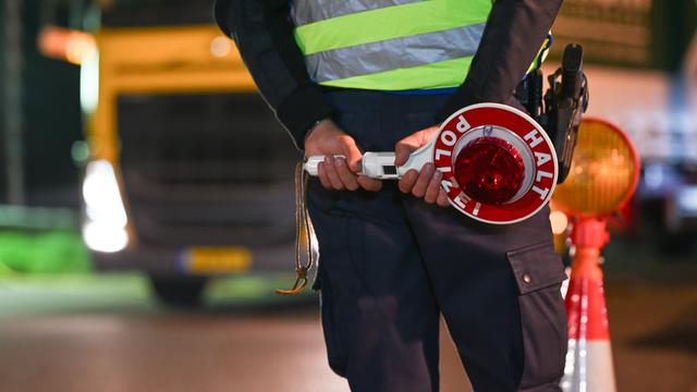 Symbol-Foto: Ein Polizist steht an einer Grenze. Im Hintergrund ist ein Last-Wagen.