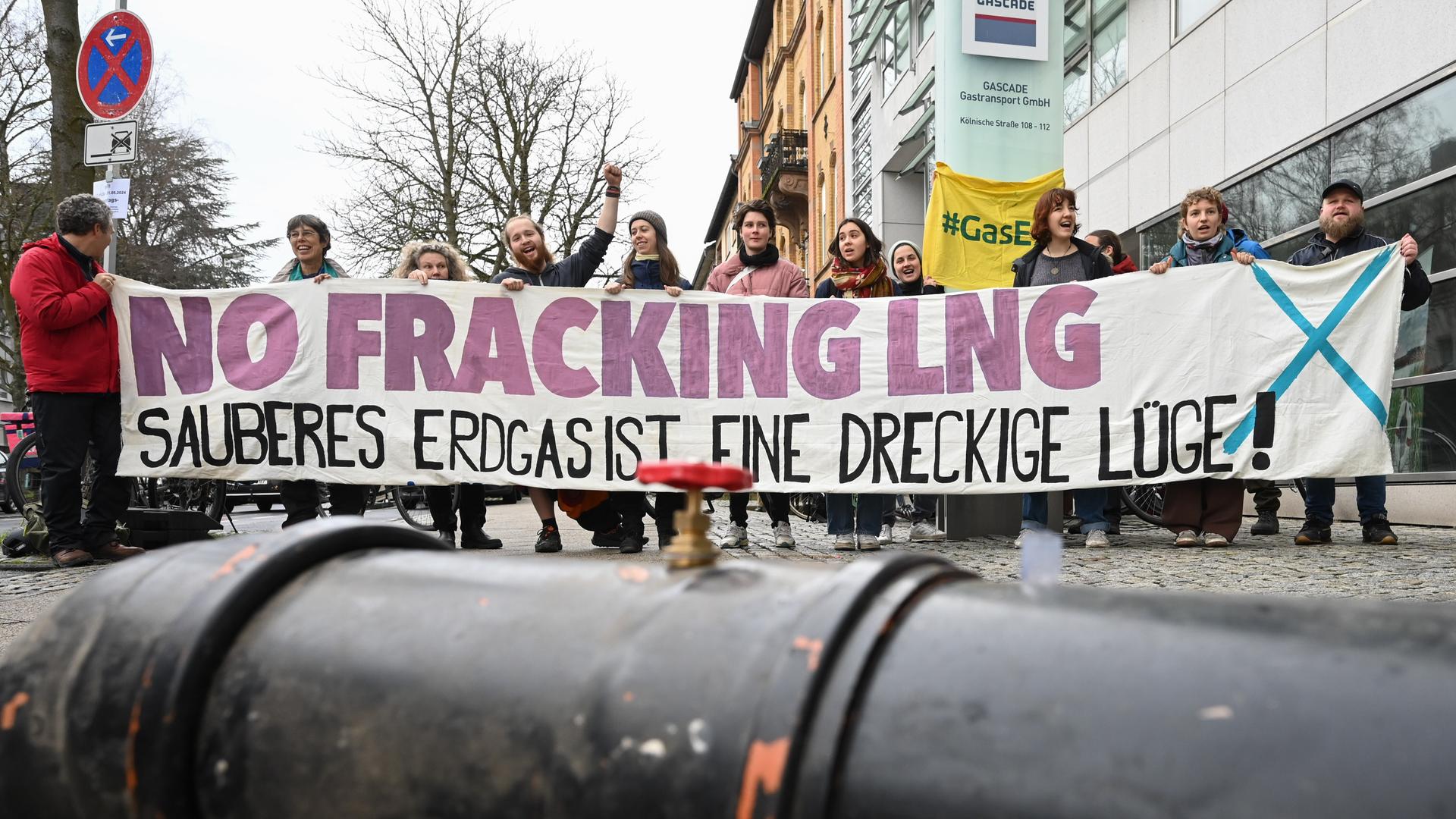 Hinter dem Abschnitt einer Pipeline demonstrieren Klimaschützer mit einem Transparent "No Fracking LNG - sauberes Erdgas ist eine dreckige Lüge!" vor der Zentrale des Gasnetzbetreibers Gascade gegen das Rügener LNG-Terminal.