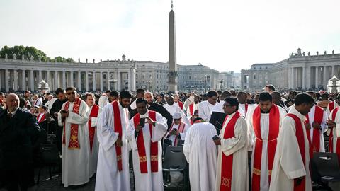 Das Bild zeigt eine Reihe von Priestern, die sich auf dem Petersplatz zu den Trauerfeierlichkeiten für den verstorbenen Papst Franziskus versammelt haben. 