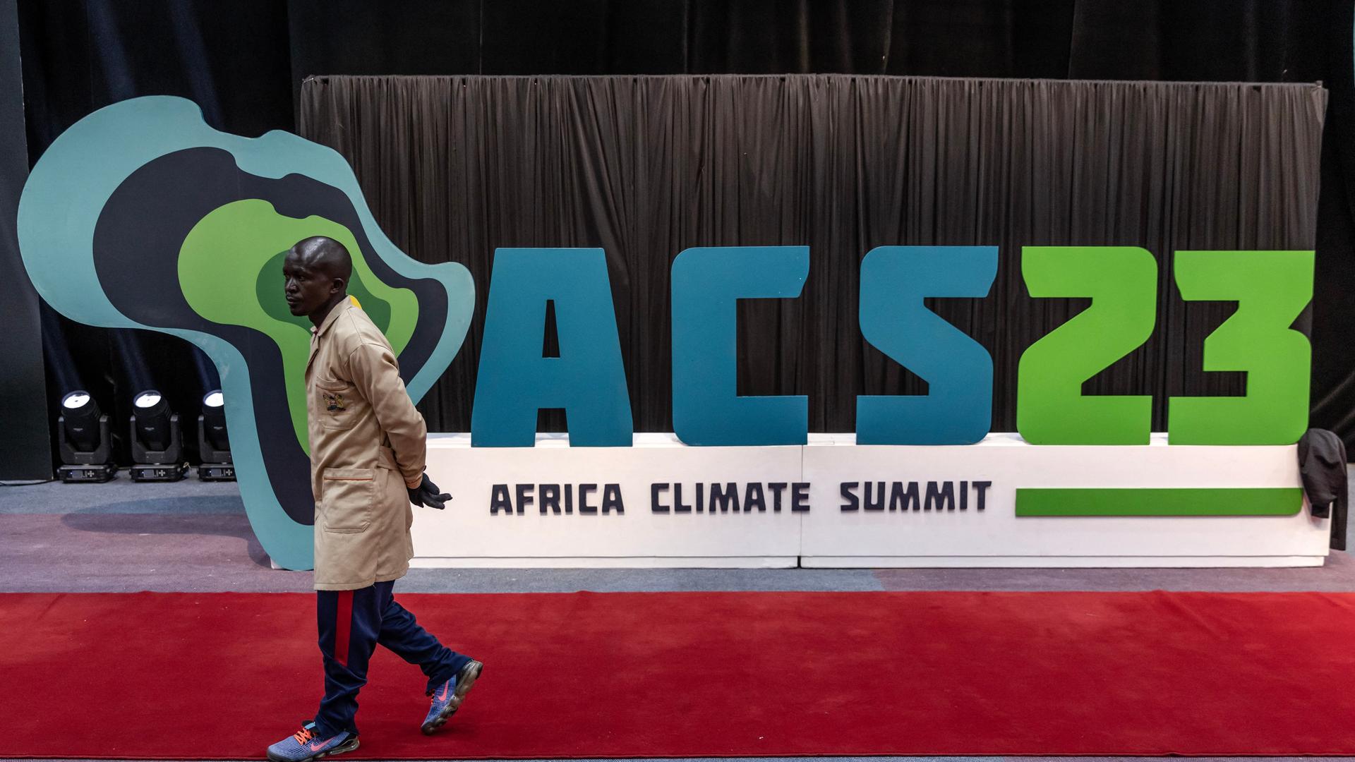 Ein Arbeiter geht auf einem roten Teppich, im Hintergrund steht ein Plakat mit dem Logo des Afrika-Klimagipfels.
