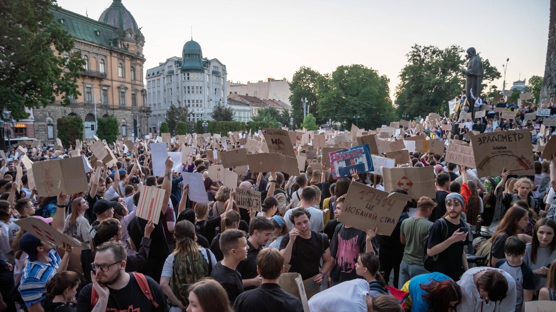 Zahlreiche Protestierende auf einem Platz, einige halten Pappschilder in die Höhe.