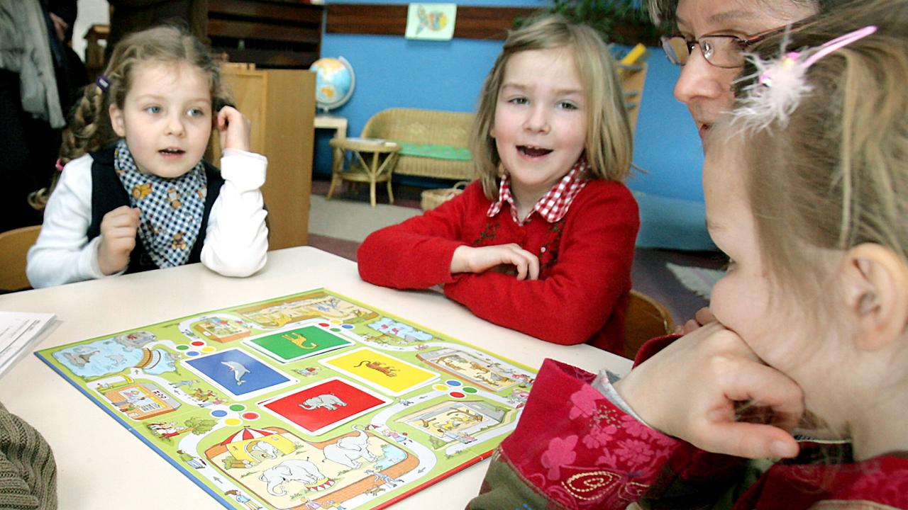 Kinder sitzen an einem Tisch um ein Brettspiel, eine Betreuerin ist auch dabei