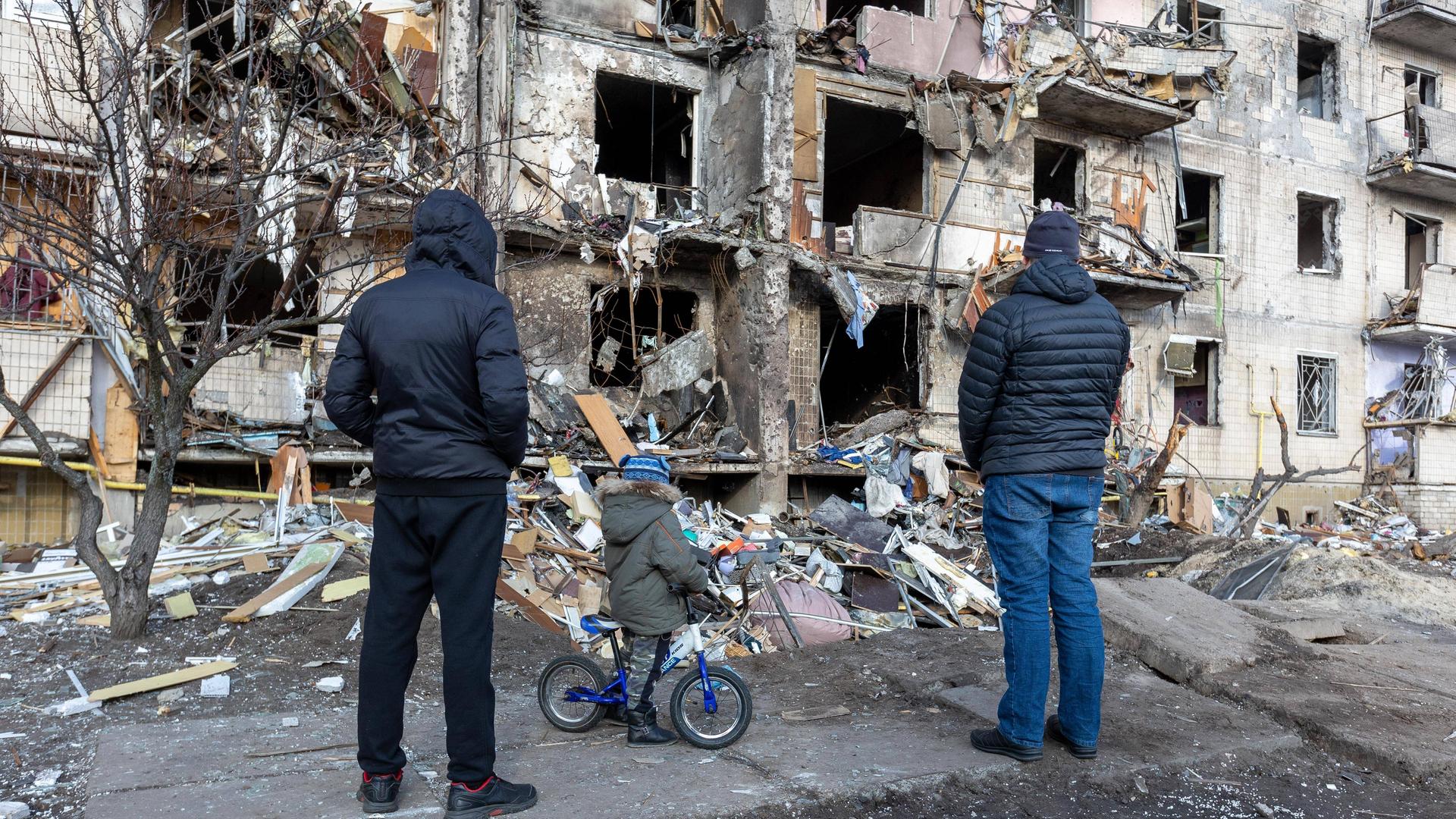 Ein zerstörtes Gebäude in Kiew nach einem russischen Bombenangriff. Menschen stehen vor dem Gebäude.