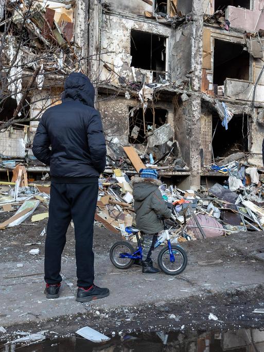 Ein zerstörtes Gebäude in Kiew nach einem russischen Bombenangriff. Menschen stehen vor dem Gebäude.