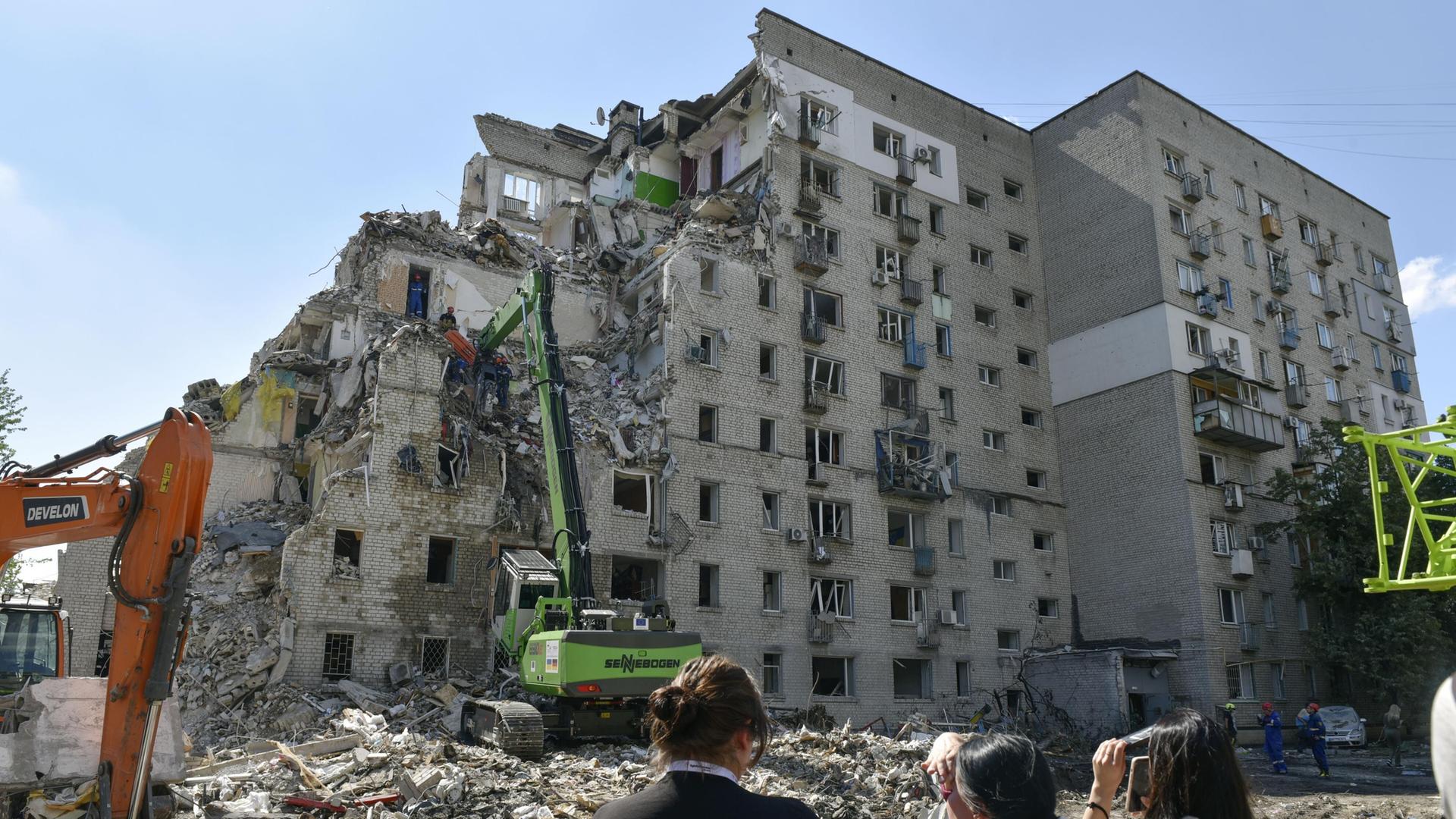 3 Frauen schauen auf ein stark zerstörtes Haus in Kiew.