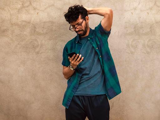 Ein Mann steht vor einer Wand und schaut auf sein Handy. Ein Mann steht vor einer Wand und schaut auf sein Handy.