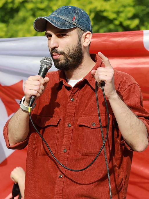 Giorgi Kakabadze steht mit einem Mikrofon in der Hand vor einer georgischen Flagge und spricht