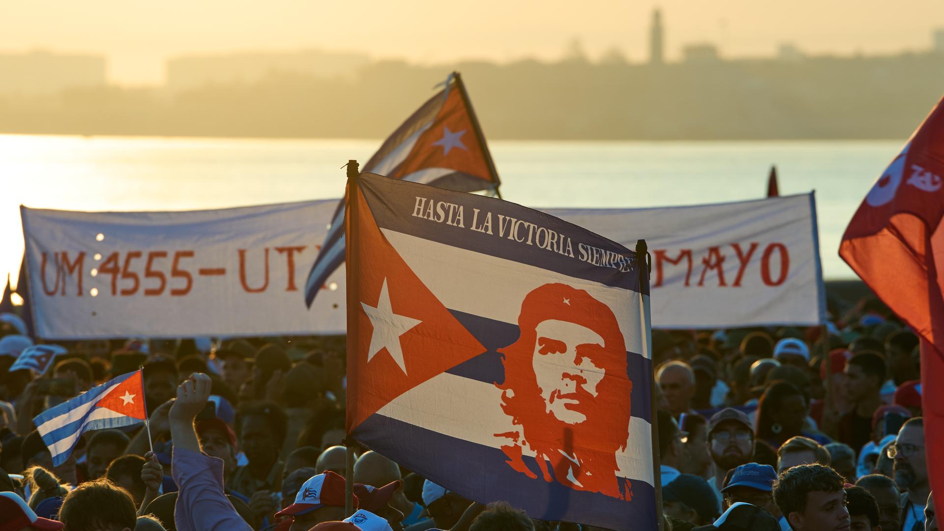 Menschen nehmen am Nachmittag an einer Veranstaltung zum Internationalen Tag der Arbeit auf Kuba teil und schwenken kubanische Fahnen, eine große zeigt das berühmte Konterfei von Che Guevara. 