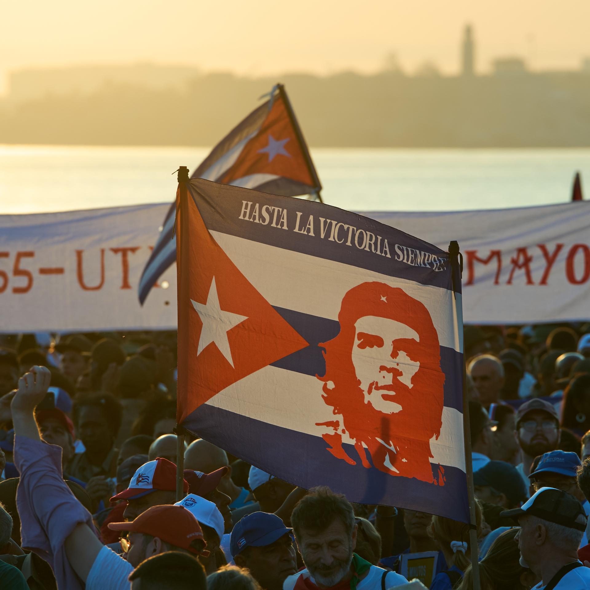 Menschen nehmen am Nachmittag an einer Veranstaltung zum Internationalen Tag der Arbeit auf Kuba teil und schwenken kubanische Fahnen, eine große zeigt das berühmte Konterfei von Che Guevara. 