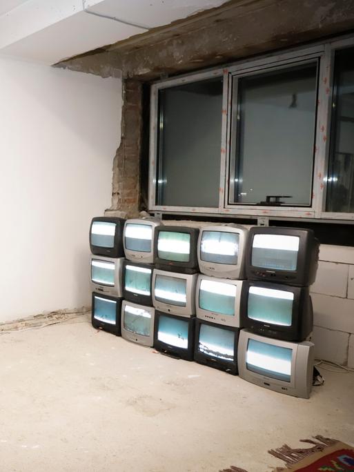 Eine Frau besucht eine Ausstellung. Sie fotografiert mit ihrem Smartphone mehrere Fernsehgeräte die aufeinandergestabelt in einem Raum stehen. Es ist die Popsängerin Dua Lipa, die die Manifesta 14 in Pristina besucht.