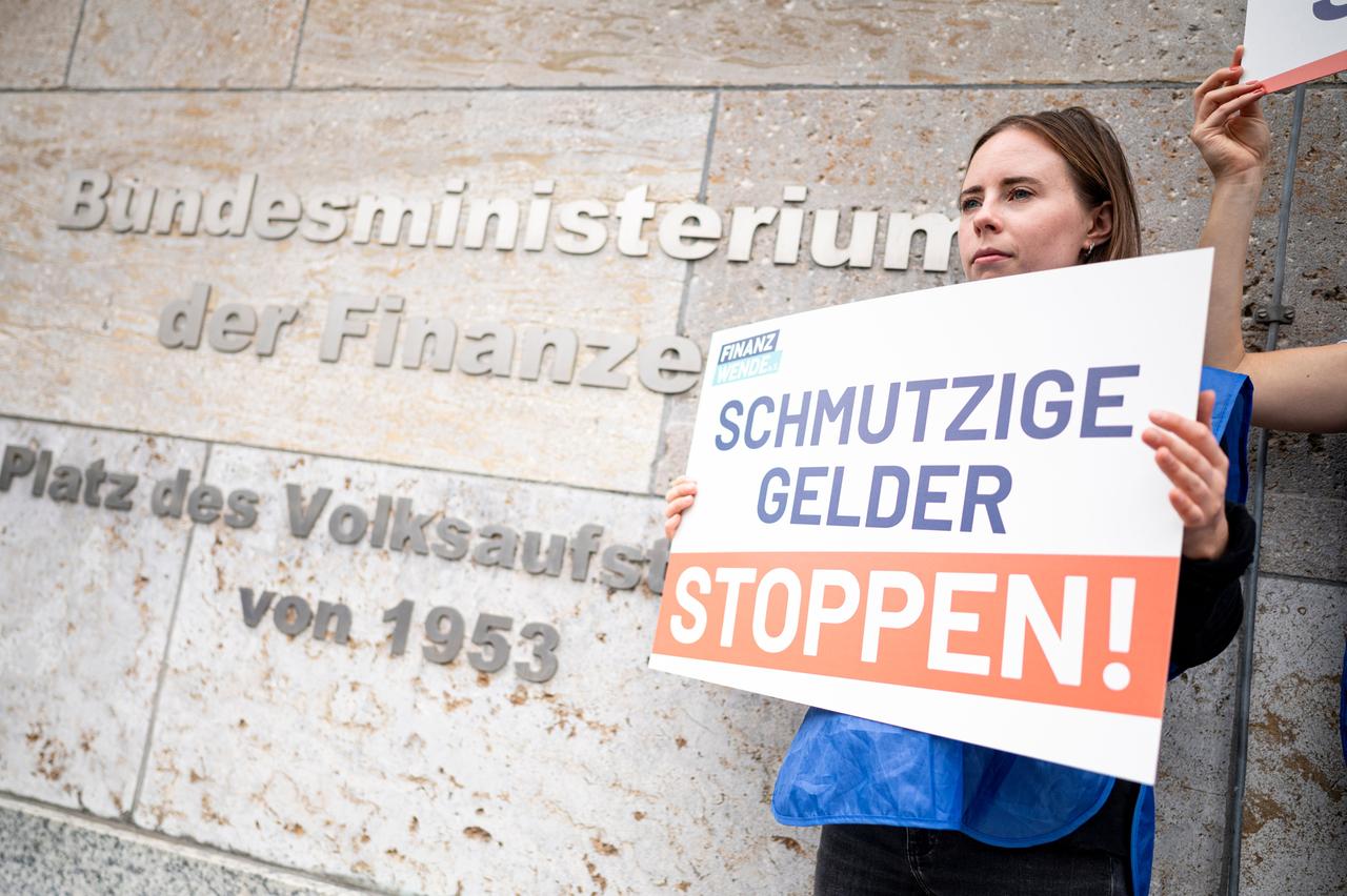 Eine Aktivistin der Bürgerbewegung Finanzwende protestiert vor dem Finanzministeriums mit einem Schild für stärkeres Vorgehen gegen schmutzige Gelder und Finanzkriminalität.