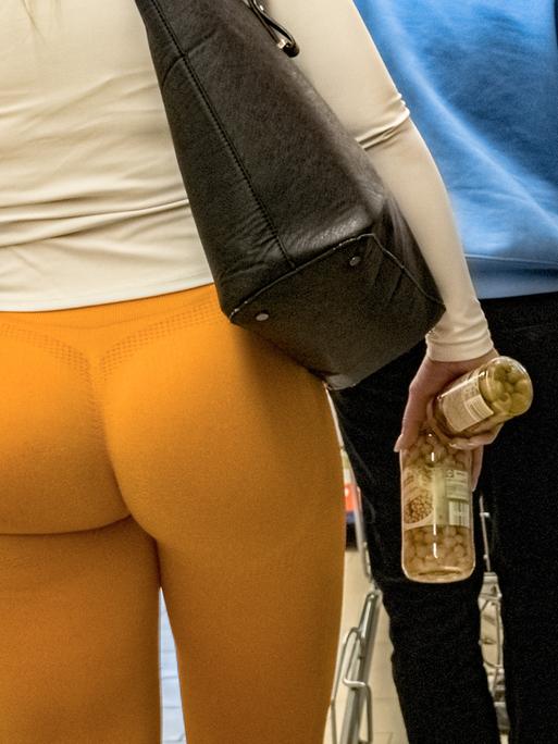 Eine Frau in Scrunch Butt Leggings steht in einem Supermarkt in der Warteschlange vor einer Kasse.