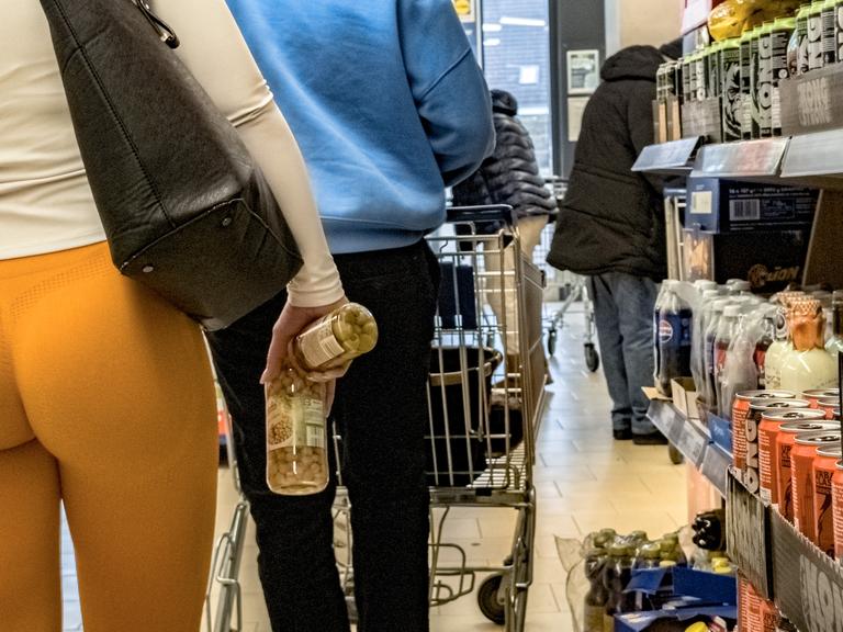 Eine Frau in Scrunch Butt Leggings steht in einem Supermarkt in der Warteschlange vor einer Kasse.