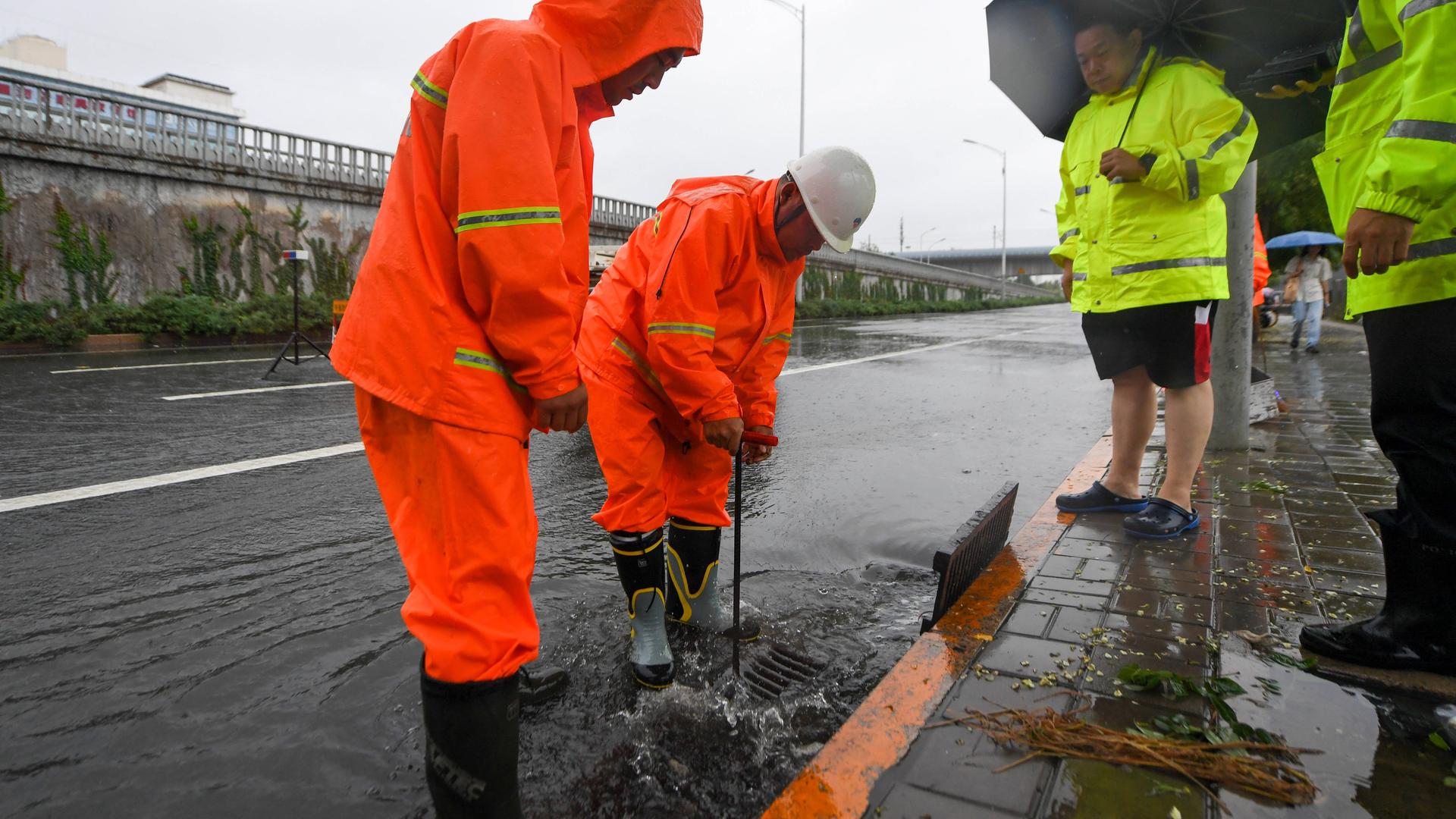 Straßenarbeiter öffnen einen Kanaldeckel, aus dem Regenwasser strömt. Straßenarbeiter öffnen einen Kanaldeckel, aus dem Regenwasser strömt.