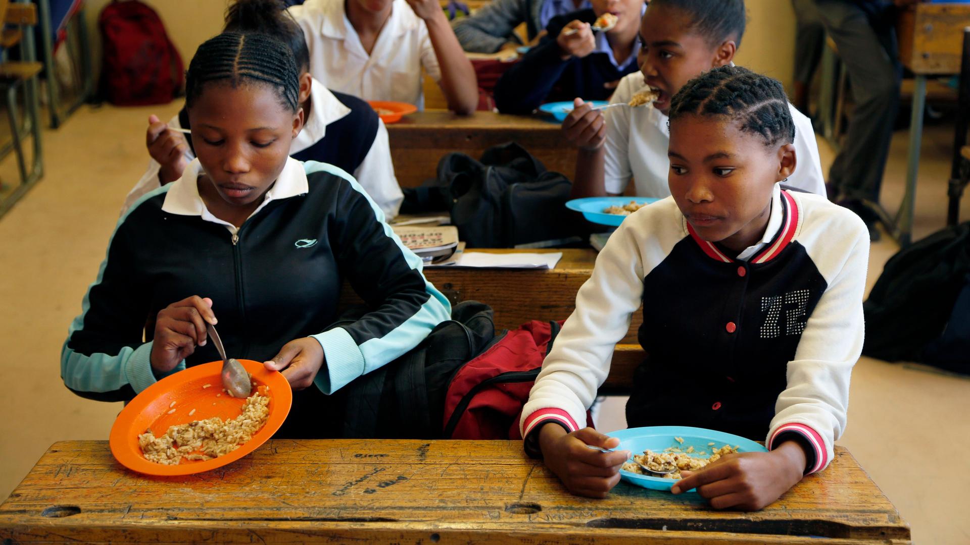 Vosburg, Südafrika: Schülerinnen essen ihr Mittagessen an den Schulbänken.