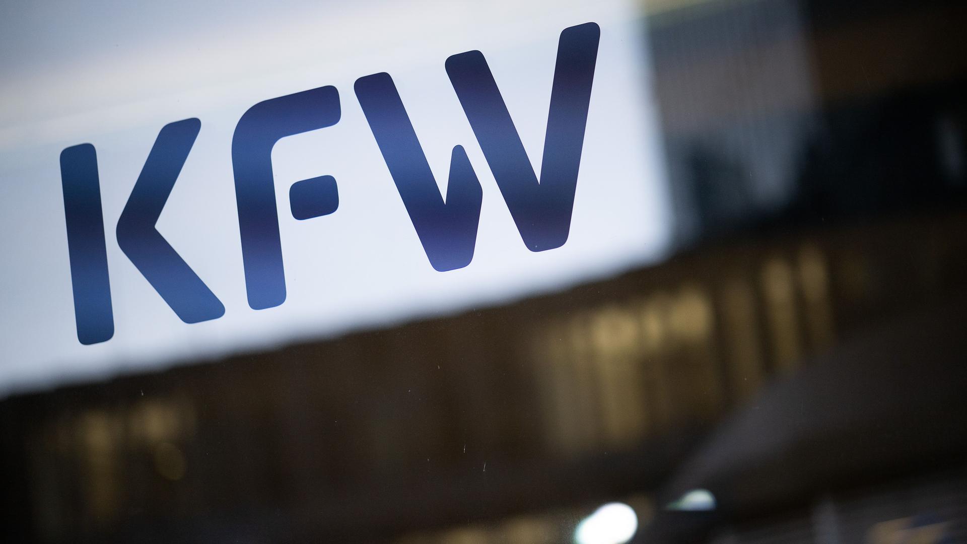 Frankfurt/Main: Das Logo der Förderbank KfW steht auf einer Glasscheibe vor Lichtern in Büros.