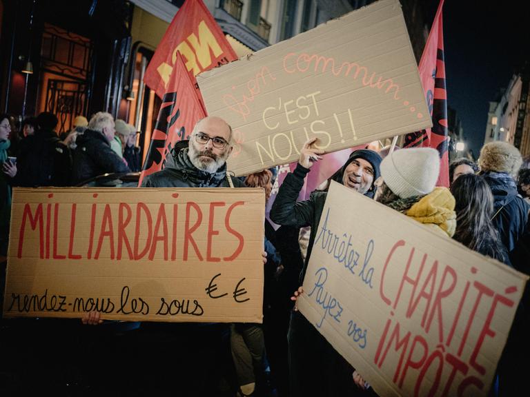 Während einer Protestaktion in Paris halten Menschen Schilder mit den Aufschriften „Milliardäre, gebt uns das Geld zurück, das Gemeinwohl sind wir" und „Hört auf mit der Wohltätigkeit, zahlt eure Steuern". Während einer Protestaktion in Paris halten Menschen Schilder mit den Aufschriften „Milliardäre, gebt uns das Geld zurück, das Gemeinwohl sind wir" und „Hört auf mit der Wohltätigkeit, zahlt eure Steuern".