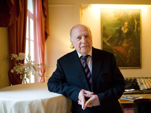 Imre Kertész lehnt sich in einem festlichen Raum an einen Stehtisch und blickt in die Kamera Imre Kertész lehnt sich in einem festlichen Raum an einen Stehtisch und blickt in die Kamera