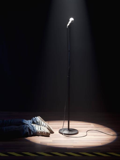 Eine Person liegt neben dem Spotlight eines Mikrofons, nur die Schuhe sind zu sehen.