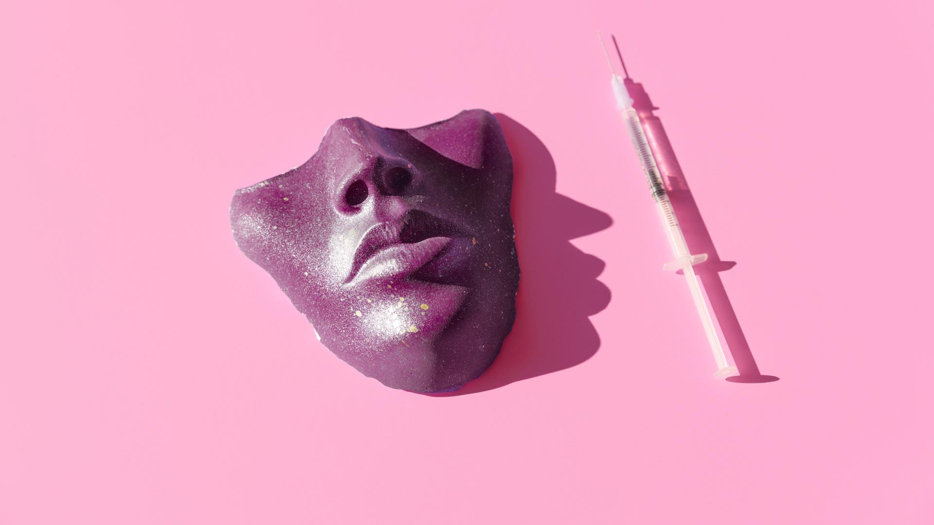 Eine Spritze und eine violette Maske vor pinkem Hintergrund