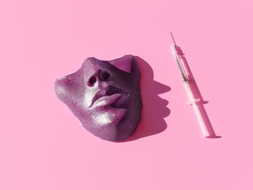 Eine Spritze und eine violette Maske vor pinkem Hintergrund