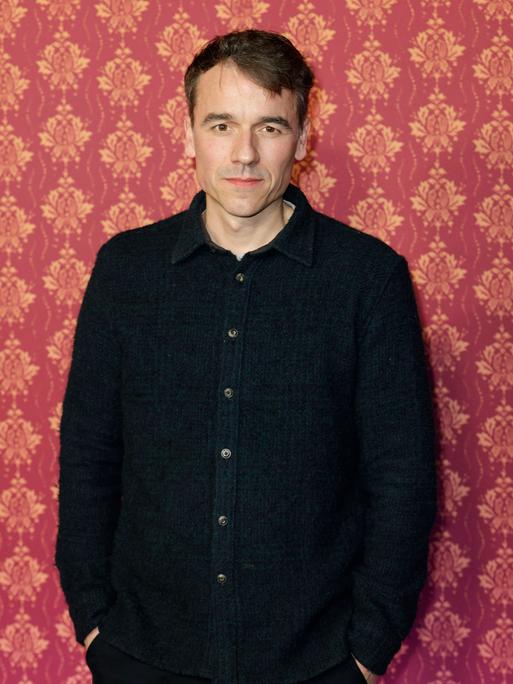 Der Schauspieler Alexander Khuon steht vor einer Tapetenwand bei der Premiere der ARD Comery-Serie "Ghosts".