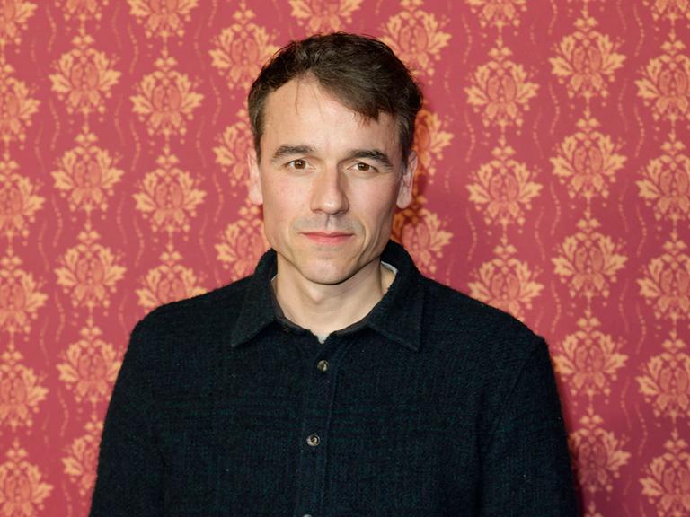 Der Schauspieler Alexander Khuon steht vor einer Tapetenwand bei der Premiere der ARD Comery-Serie "Ghosts".