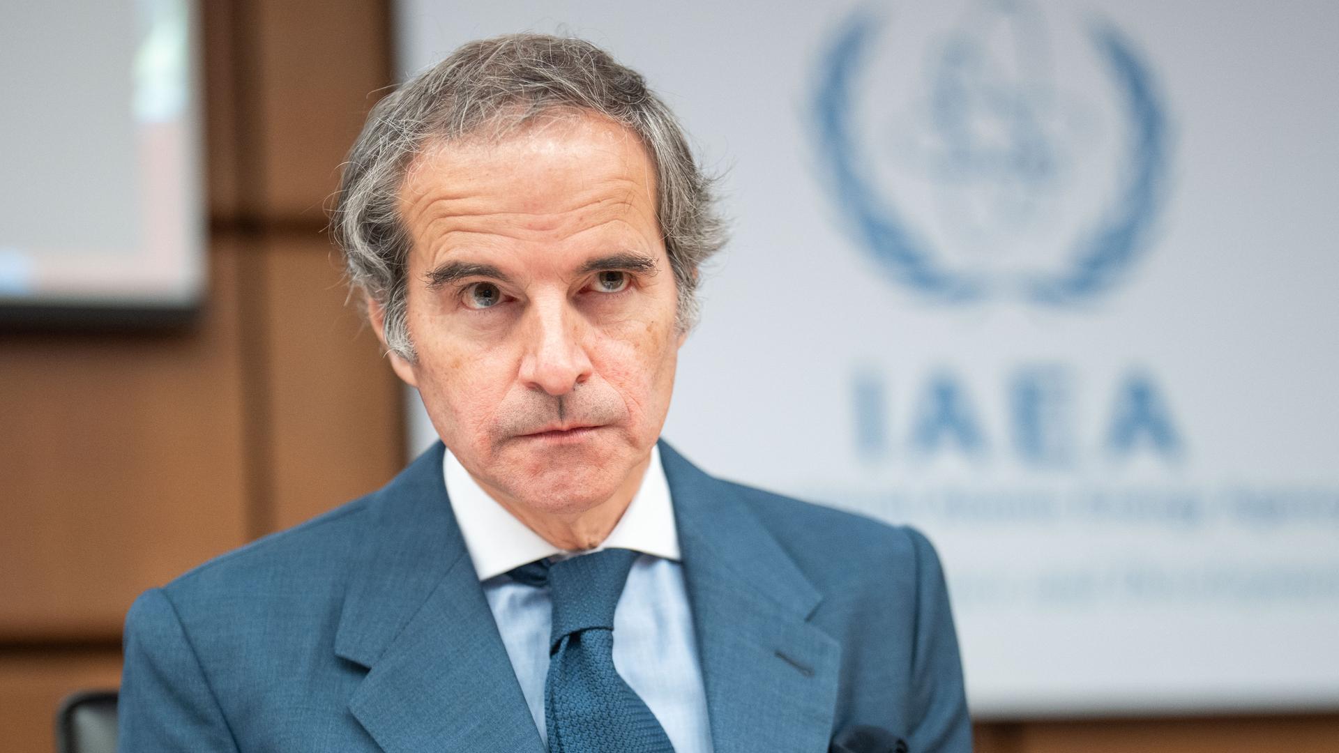 Das Bild zeigt Rafael Grossi. Im Hintergrund ist ein großes Logo der Internationalen Atomenergiebehörde zu sehen.