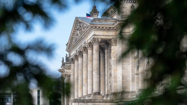 Blick durch Bäume auf die Front des Reichstags in Berlin.