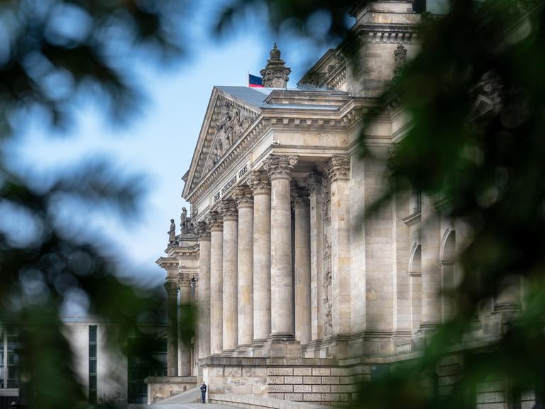 Blick durch Bäume auf die Front des Reichstags in Berlin.