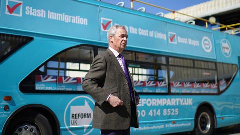 Nigel Farage steht während seiner Wahlkampftour vor einem hellblauen Werbebus seiner Partei Reform UK.