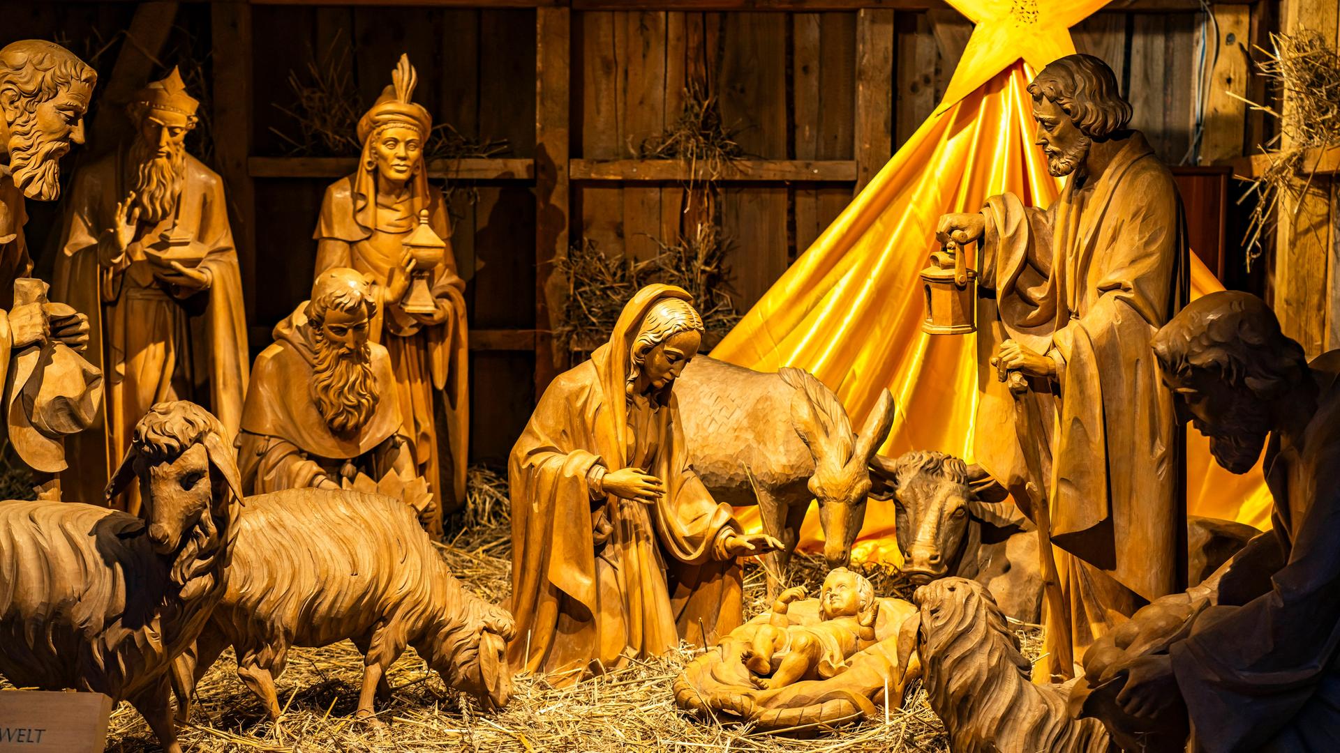 Eine Weihnachtskrippe aus hölzernen Figuren: das Jesuskind umgeben von Mutter Maria, Josef, den heiligen drei Königen, zwei Schafen und einem Stern über ihren Köpfen