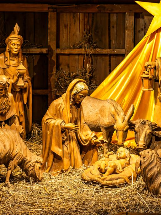 Eine Weihnachtskrippe aus hölzernen Figuren: das Jesuskind umgeben von Mutter Maria, Josef, den heiligen drei Königen, zwei Schafen und einem Stern über ihren Köpfen