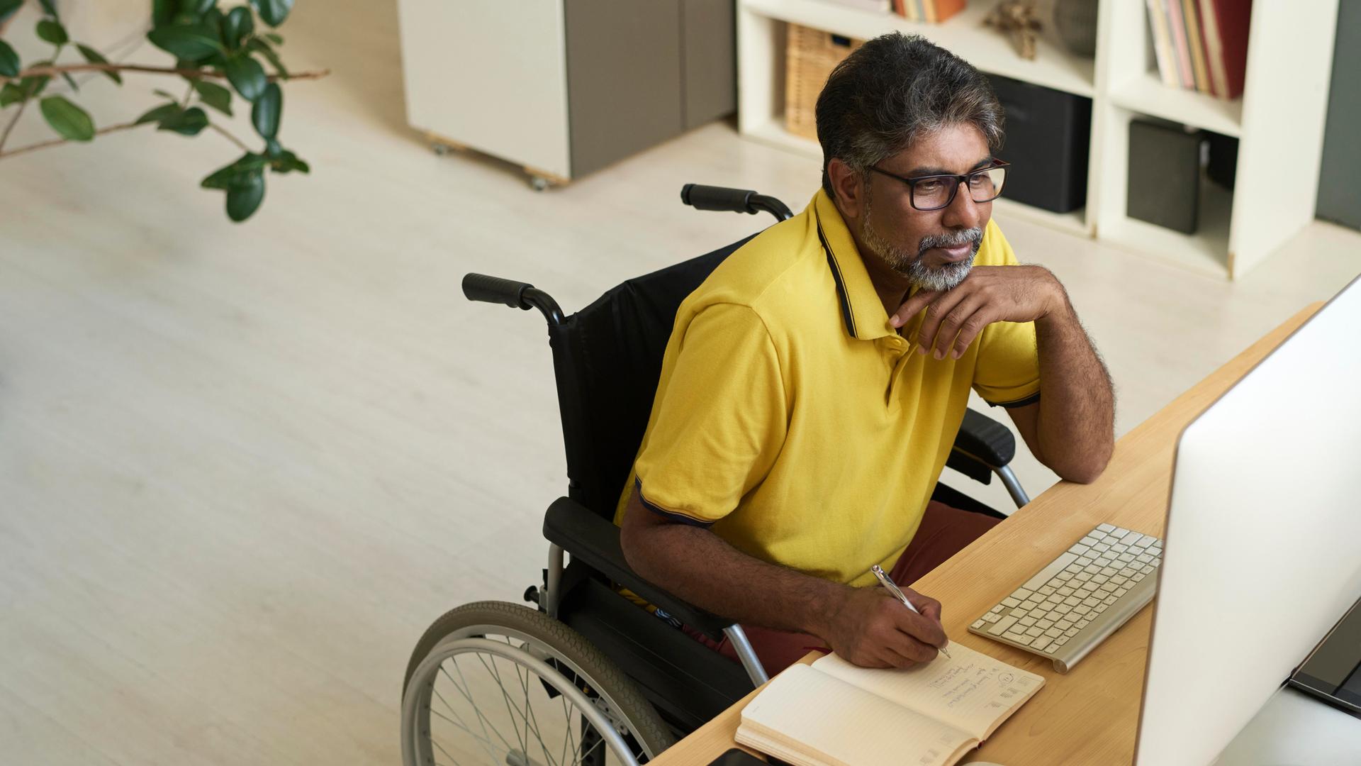 Ein Mensch im Rollstuhl nutzt einen Computer. Ein Mensch im Rollstuhl nutzt einen Computer.