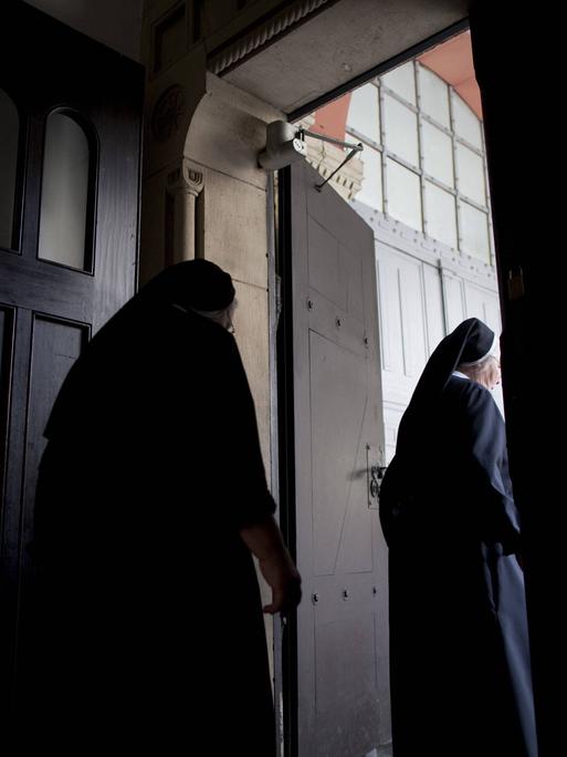 Zwei Ordensfrauen in dunklen Gewändern gehen durch eine Tür.