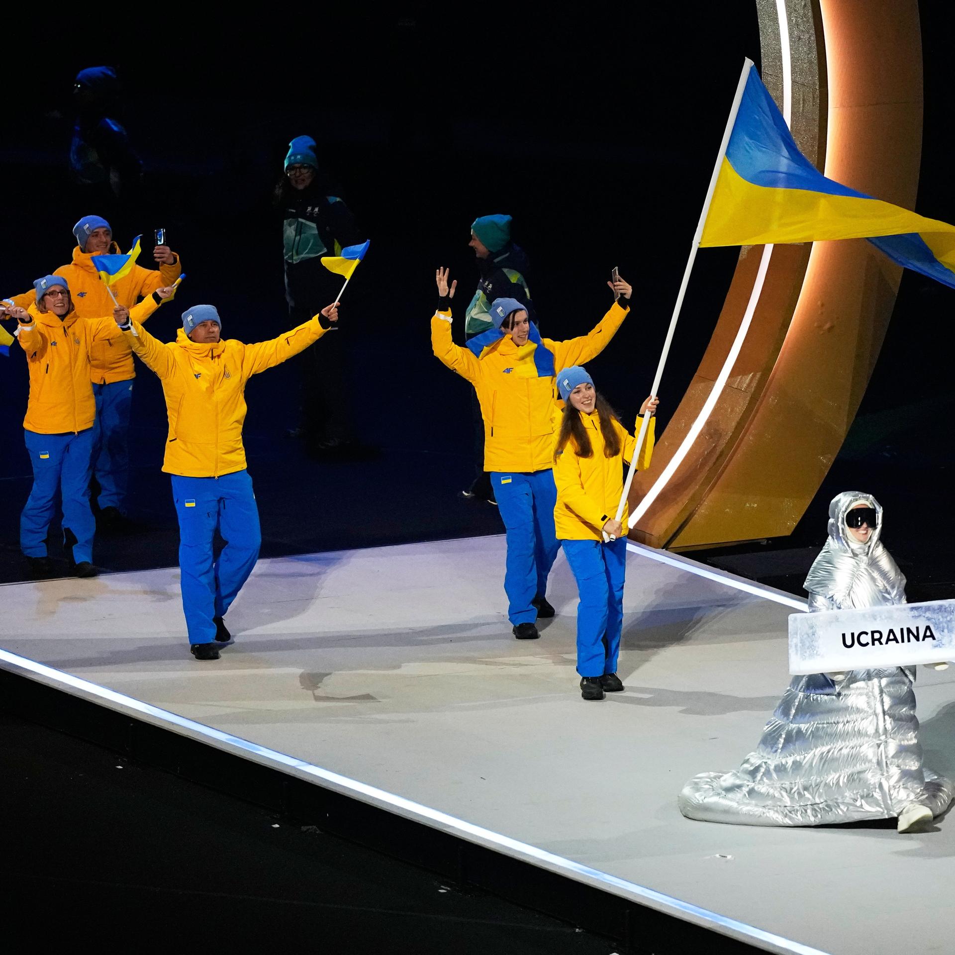 Olympische Winterspiele Mailand Cortina 2026,  Anastasia Kutscherowa trägt das Schild, als sie die Athleten aus der Ukraine bei der Eröffnungsfeier der Olympischen Winterspiele in die Arena führt.