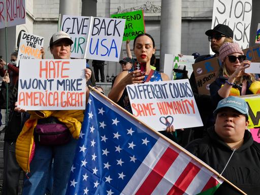 Menschen protestieren und halten Schilder. Auf einem steht "Hate won't make America great again". Die Proteste richten sich gegen die Politik Donald Trumps. Die Menschen stehen vor dem Rathaus in Los Angeles.